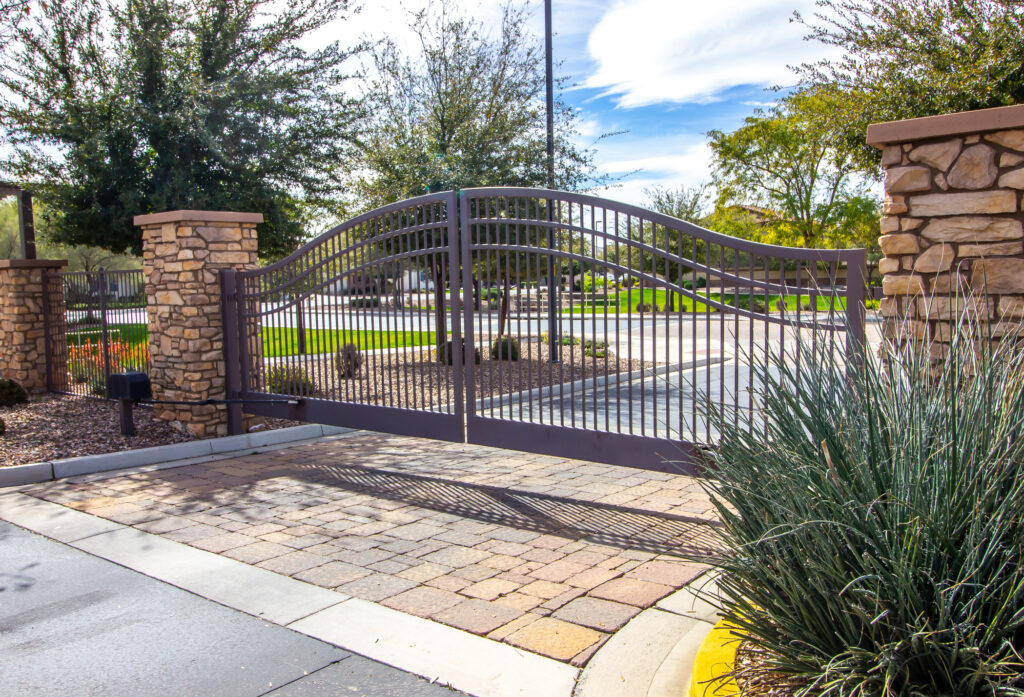 A wrought iron security gate with rock columns is pictured at the driveway entrance of a large residential property.