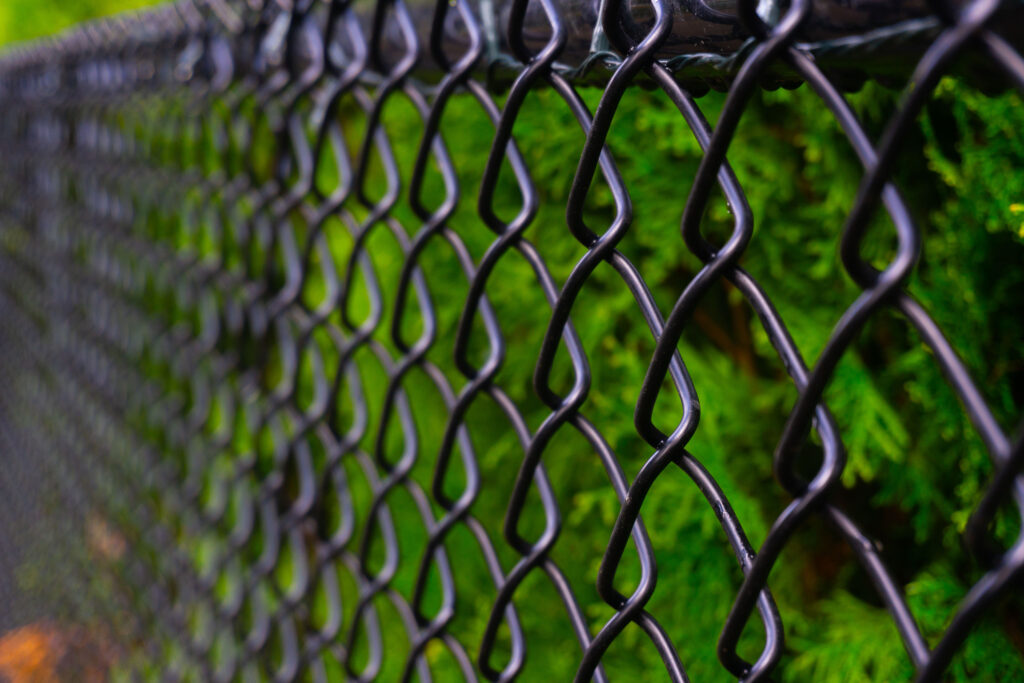 Close-up of a black chain link fence in a backyard.