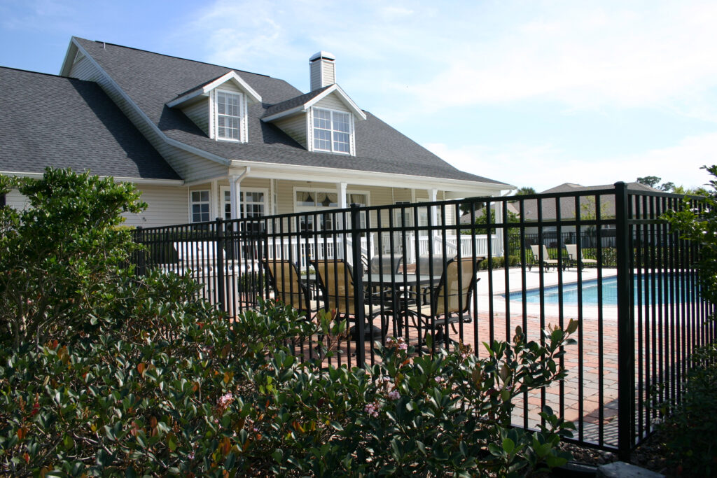 A dark wrought iron pool fence surrounding a residential pool in a home’s backyard.