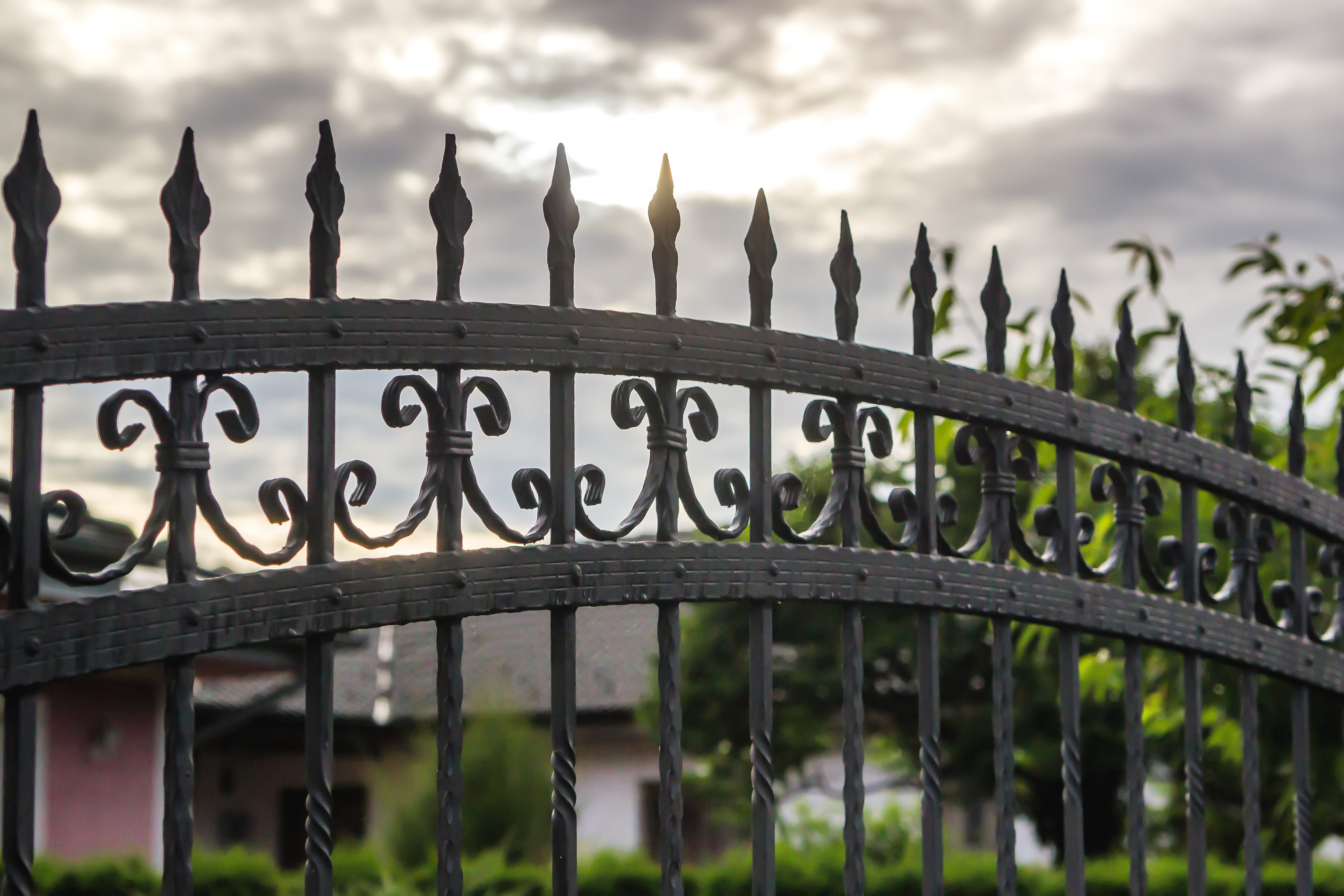 Close-up of an ornate black wrought iron fence on a residential property on a cloudy day.