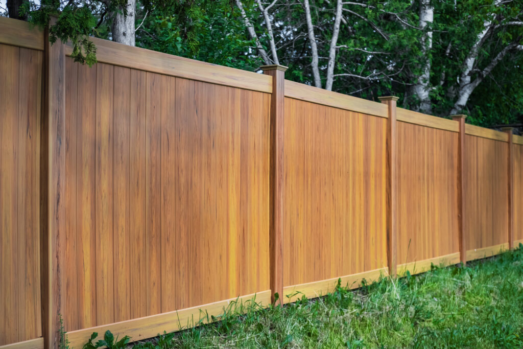 Portion of a new wooden fence around a house with trees on the other side. 