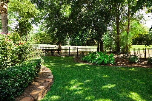 A black wrought iron fence lines separates a well-maintained lawn and garden area from other property.