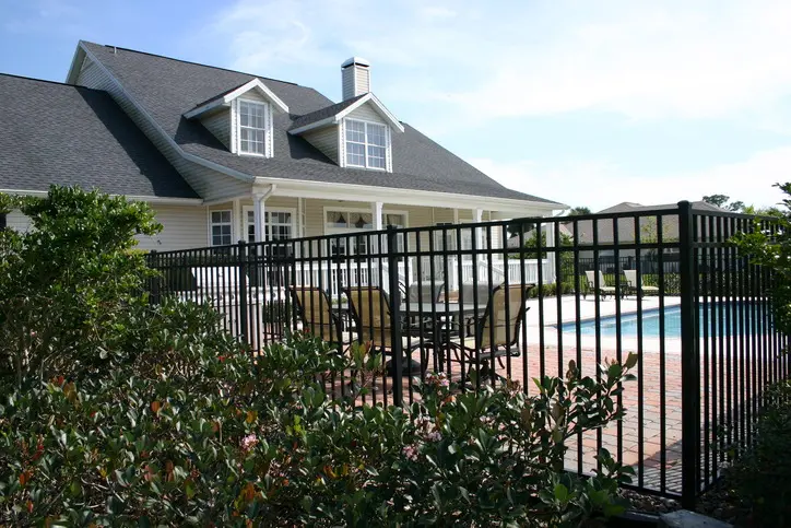 GettyImages-144328141 (1) A modern black wrought iron fence surrounding a backyard pool area at a suburban home, providing safety while complementing the home's landscaping and outdoor living space.