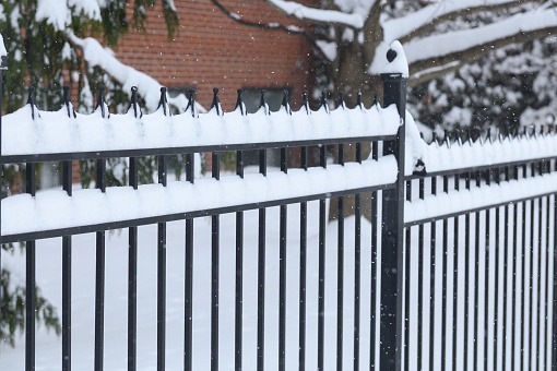 image Black wrought iron fence covered in snow during a Canadian winter, showing durability and low maintenance in cold weather.