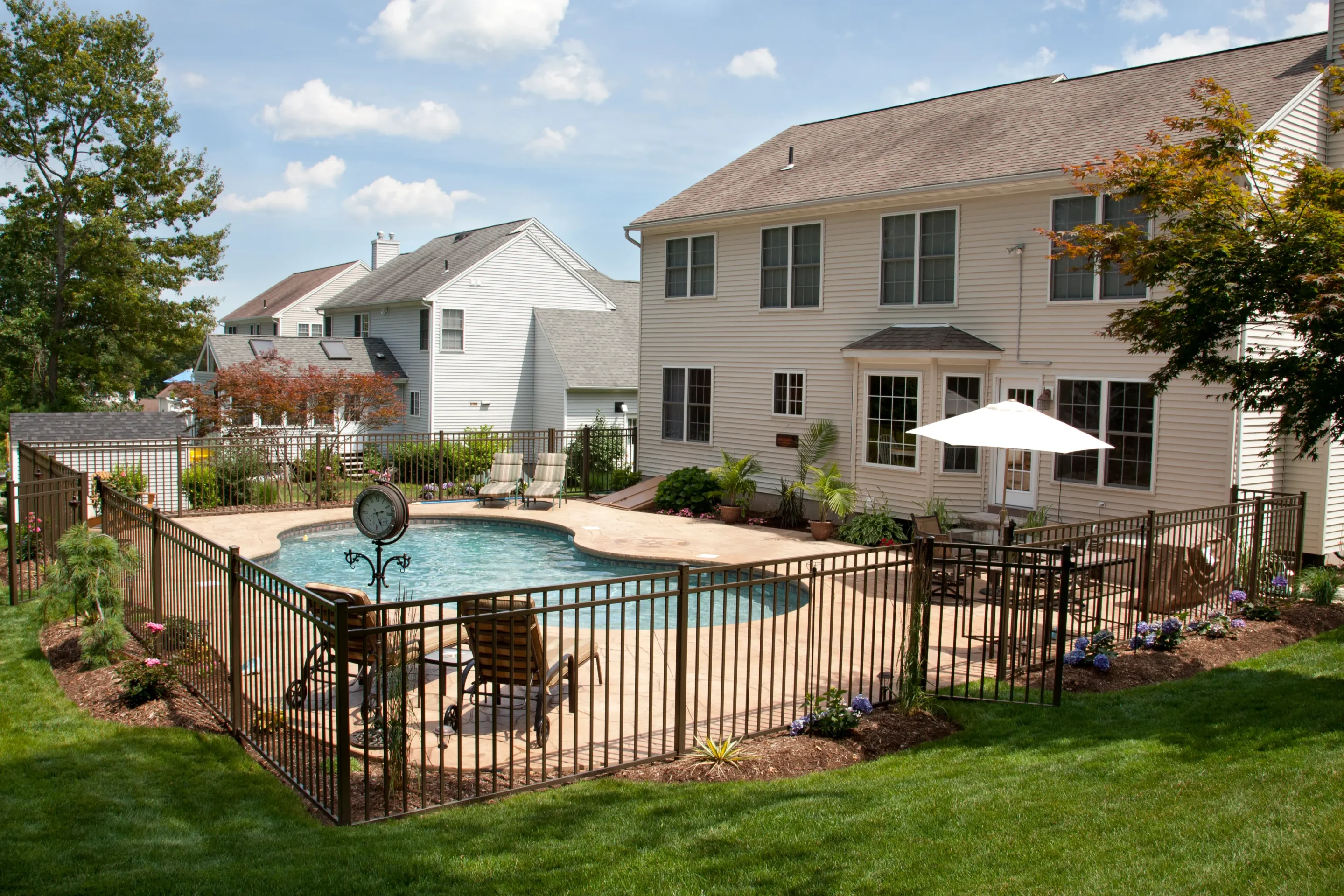 Black wrought iron fence around a kidney-shaped in-ground pool in an Ontario backyard with patio seating and umbrella.